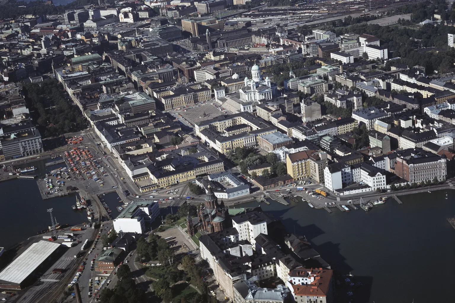 Kädet pitelevät älypuhelinta kahvilan pöydän ääressä, taustalla sumea kaupunkinäkymä